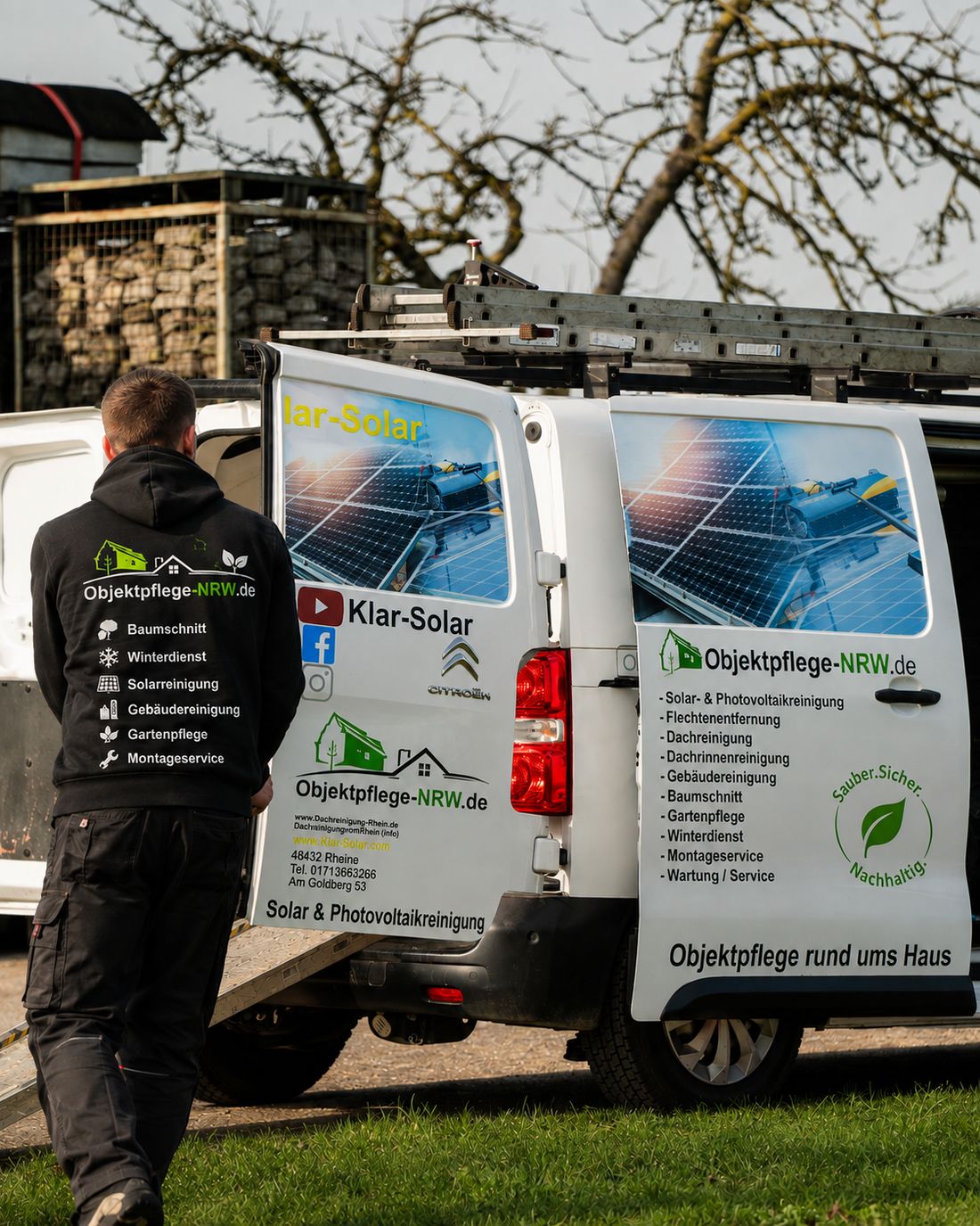 Mitarbeiter in Arbeitskleidung geht auf den beschrifteten Firmentransporter zu, Heckklappe geöffnet